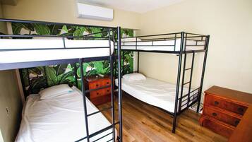 A bunk bed room with a wooden floor, a small dresser, and a wall with a tropical wallpaper.