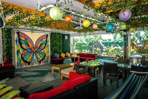A room with a large butterfly mural, red and black wicker furniture, and a view of greenery outside. - Waikiki Beachside Hostel (Honolulu)