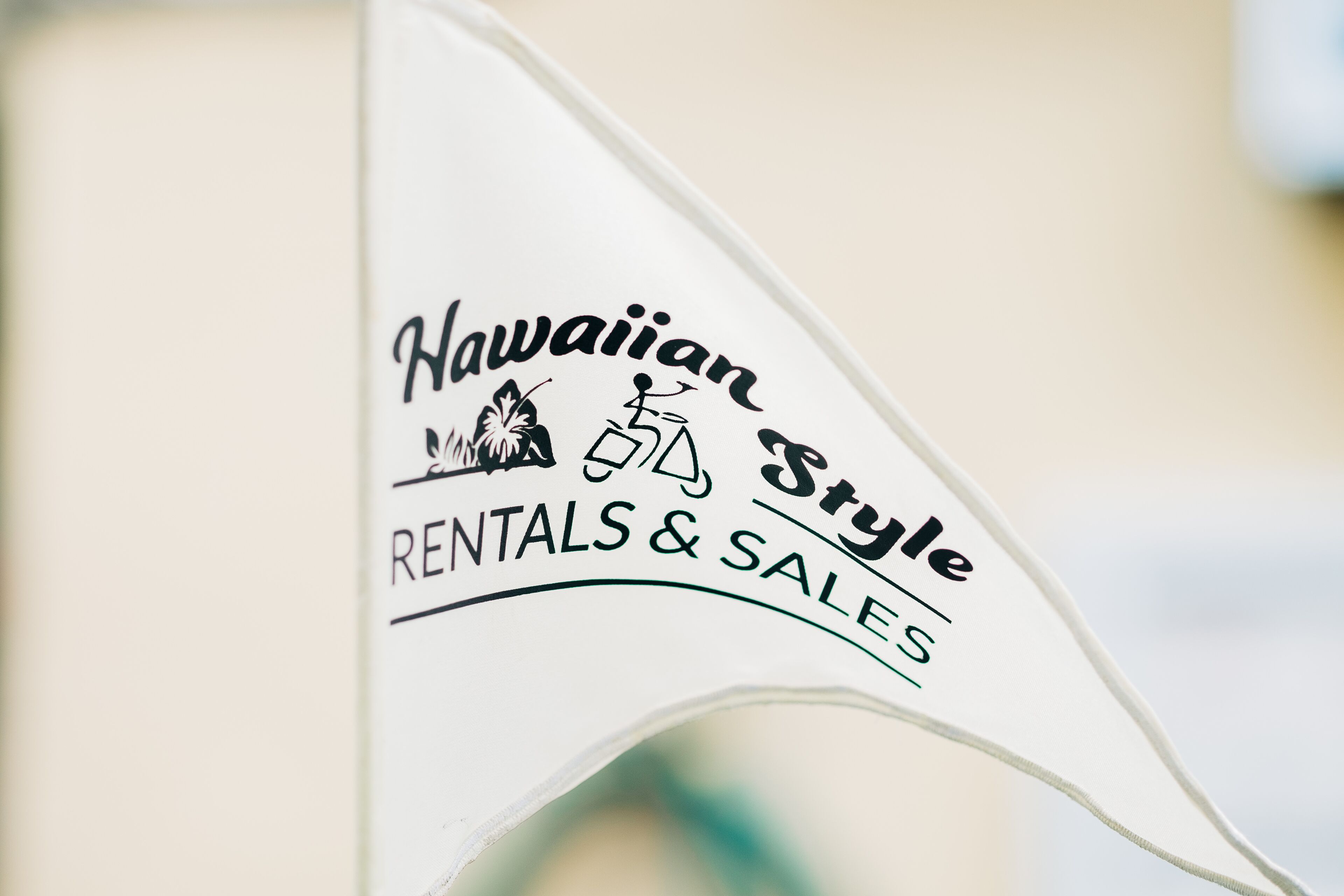 Uma bandeira com o texto 'Hawaiian Style Rentals & Sales' e um ícone de montanha e prancha de surf.