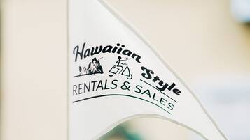 Uma bandeira com o texto 'Hawaiian Style Rentals & Sales' e um ícone de montanha e prancha de surf.