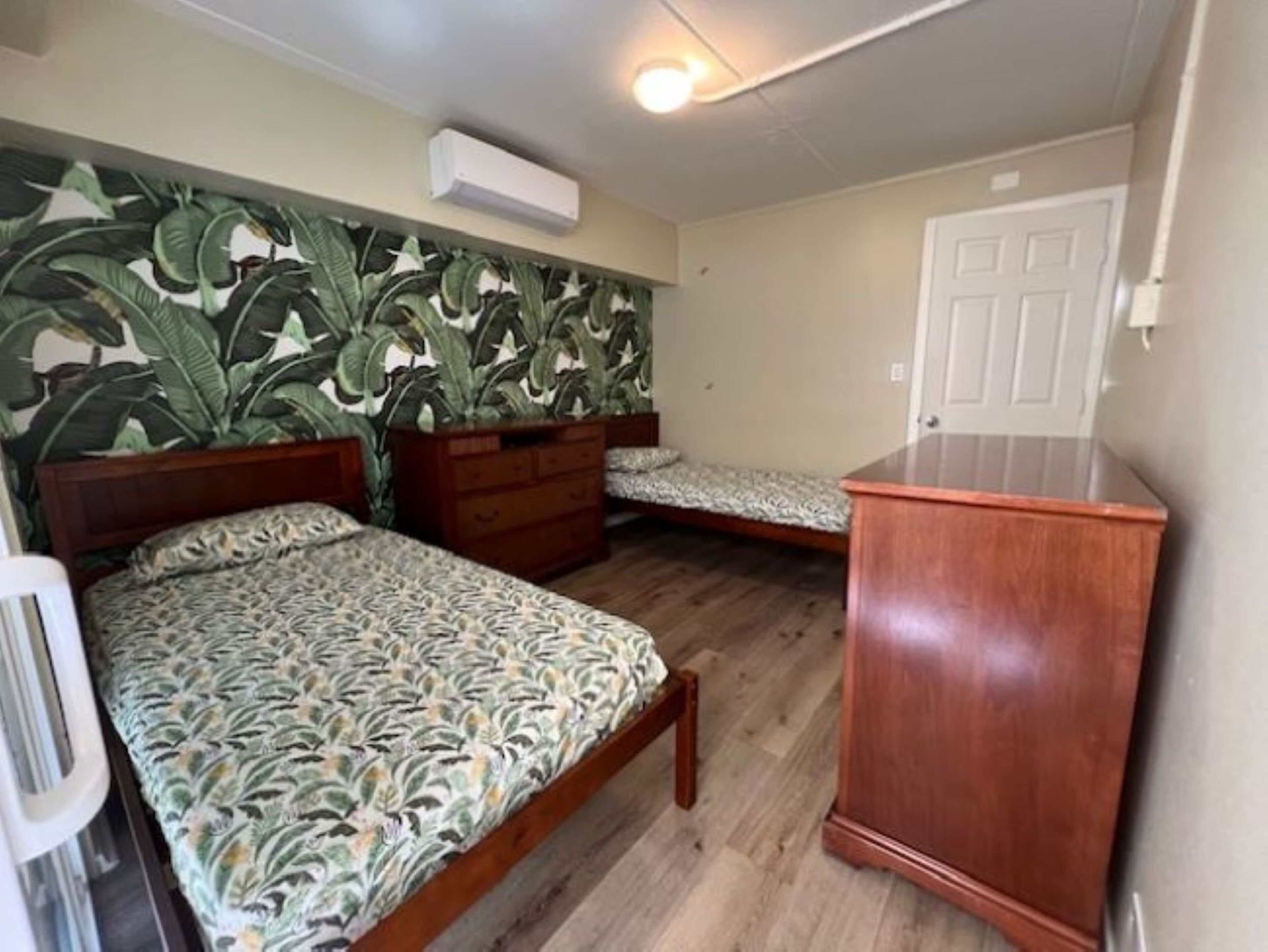A room with two beds, a wooden dresser, and a wall with a tropical leaf pattern.