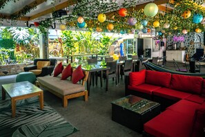A cozy indoor seating area with a red sofa, a wooden table, and a green patterned rug. - Waikiki Beachside Hostel (Honolulu)