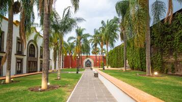 A courtyard with a paved walkway, palm trees, and a building with arched windows and a red wall.