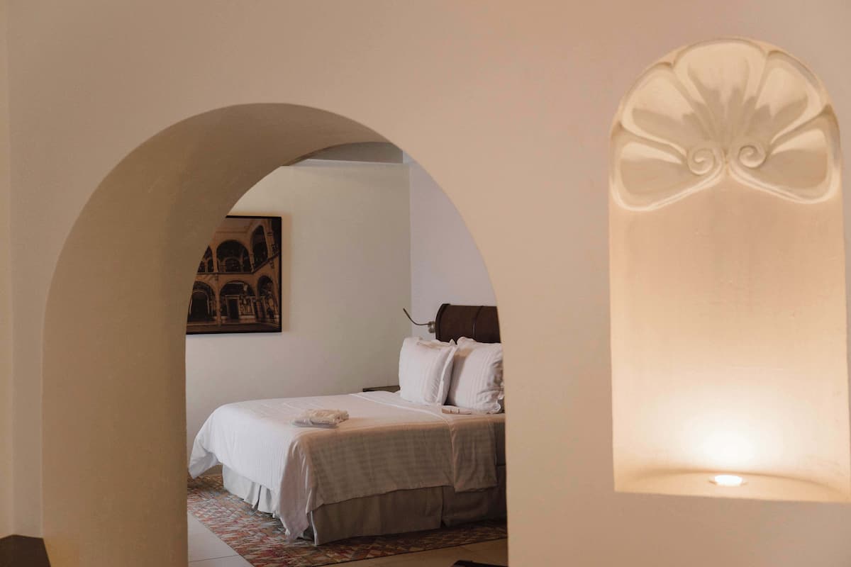 Une chambre à coucher avec un lit, une arche décorative sur un mur et un luminaire fixé au mur.