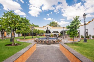 A courtyard with a fountain, surrounded by trees and a building with a distinctive architectural style.