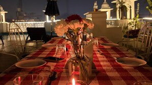 A table set for two with a red and white checkered tablecloth, a candle, and a vase with flowers. - Hotel Atulyaa Taj (Agra)
