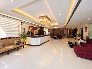 A hotel lobby with a reception desk, sofas, a chandelier, and decorative wall art. - Hotel Atulyaa Taj (Agra)
