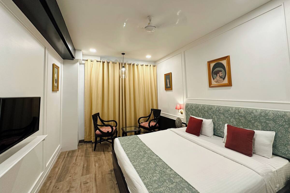 A hotel room with a bed, two chairs, a desk, a TV, and a curtain.