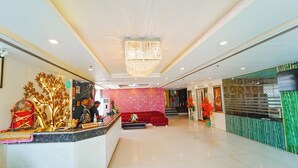A hotel reception area with a marble counter, a reception desk, a red sofa, and a chandelier. - Hotel Atulyaa Taj (Agra)