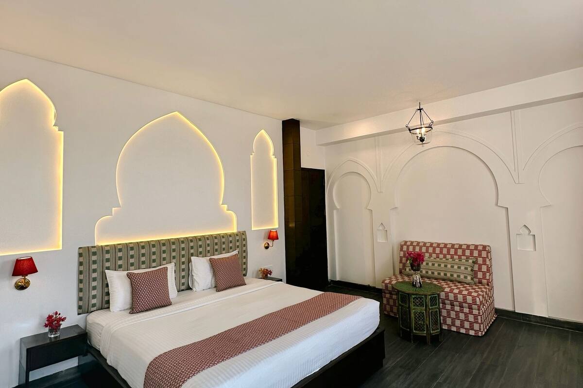 A modern hotel room with a large bed, a small table with a chair, and decorative wall lighting.