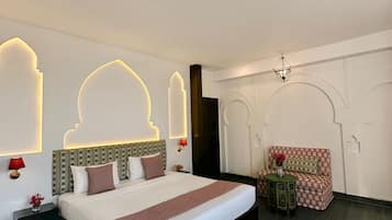 A modern hotel room with a large bed, a small table with a chair, and decorative wall lighting.