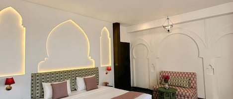 Una habitación de hotel moderna con una cama grande, una pequeña mesa con una silla e iluminación decorativa en la pared.