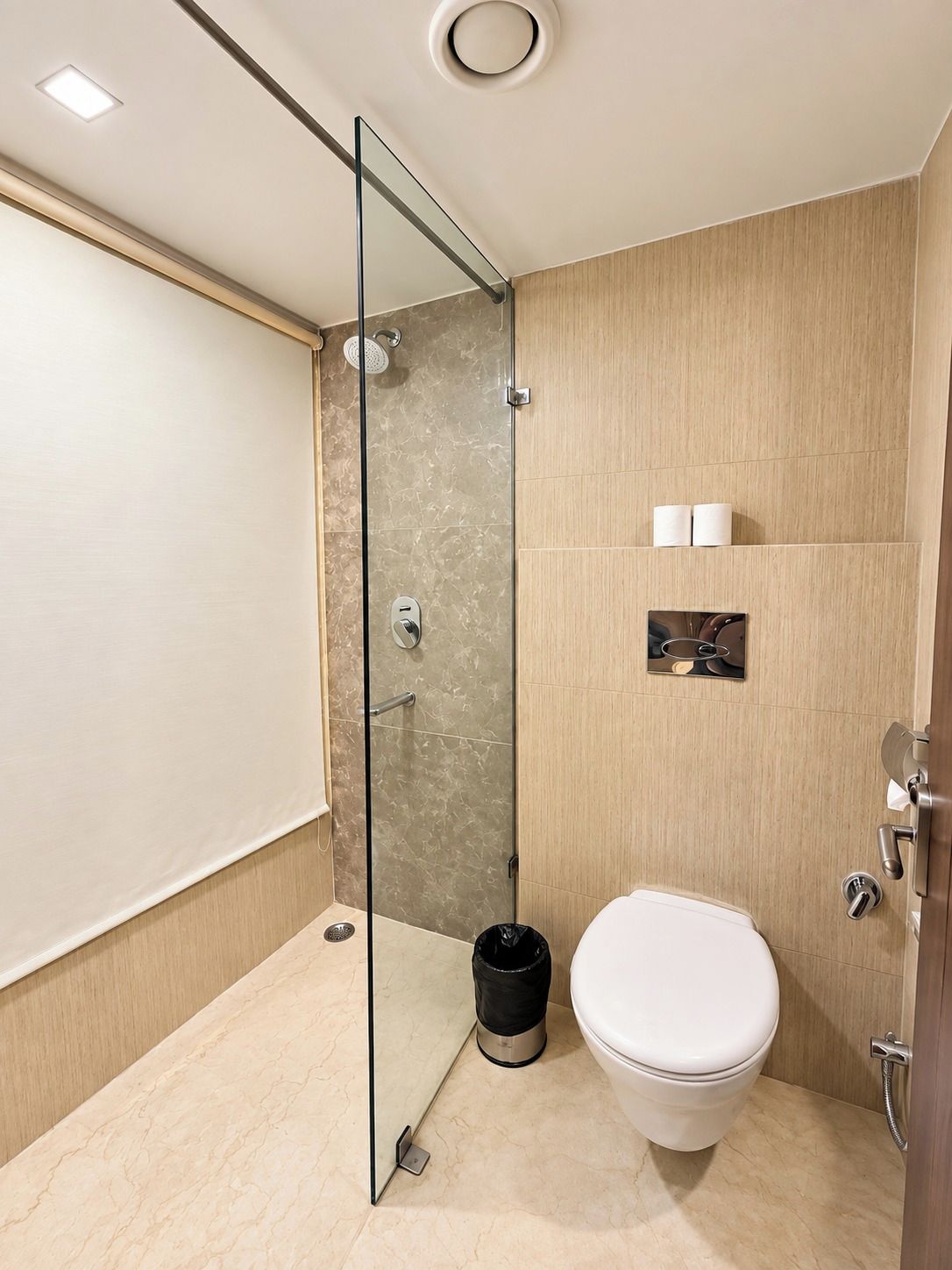 A modern bathroom with a glass shower enclosure, a toilet, and a small shelf with toiletries.