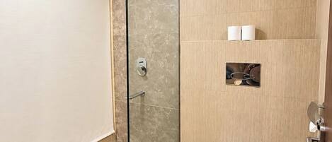 A modern bathroom with a glass shower enclosure, a toilet, and a small shelf with toiletries.