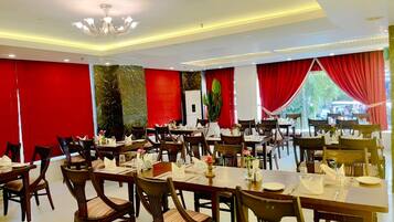 A dining area with multiple tables and chairs, red curtains, and a chandelier.