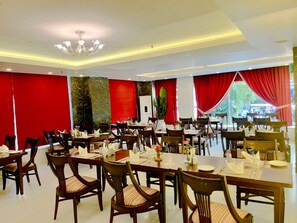 A dining area with multiple tables and chairs, red curtains, and a chandelier. - Hotel Atulyaa Taj (Agra)