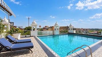 A rooftop pool with clear blue water, surrounded by lounge chairs and a patterned floor.