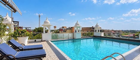 A rooftop pool with clear blue water, surrounded by lounge chairs and a patterned floor.