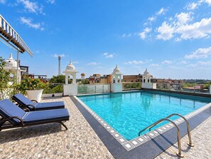 A rooftop pool with clear blue water, surrounded by lounge chairs and a patterned floor. - Hotel Atulyaa Taj (Agra)