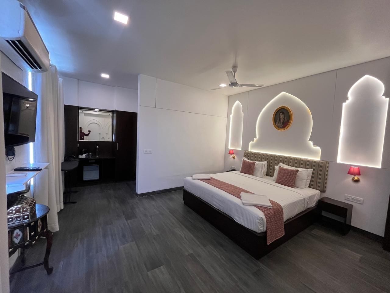 A modern hotel room with a large bed, bedside lamps, a ceiling fan, and a small desk area.