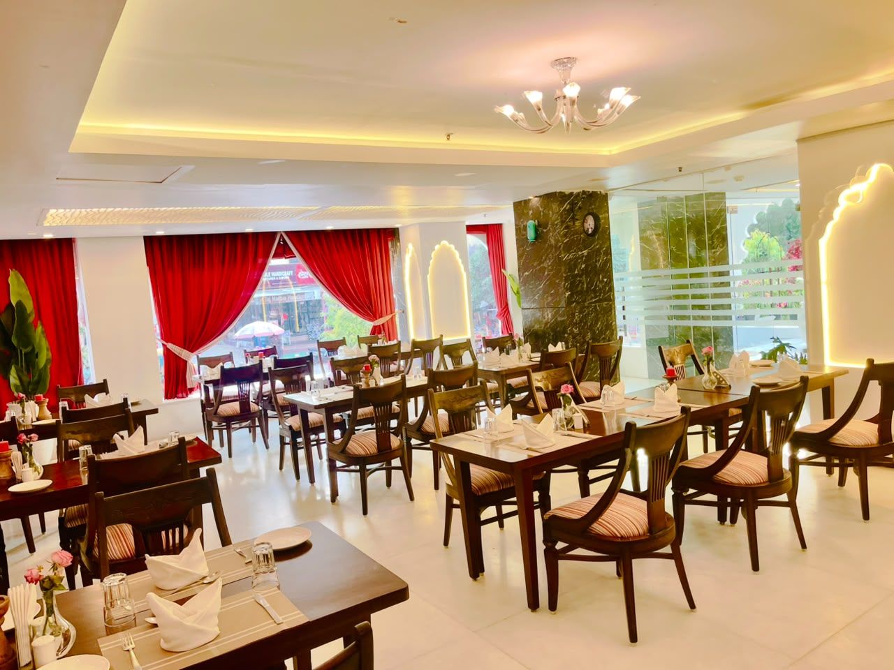 A restaurant with multiple dining tables and chairs, red curtains, and a chandelier.