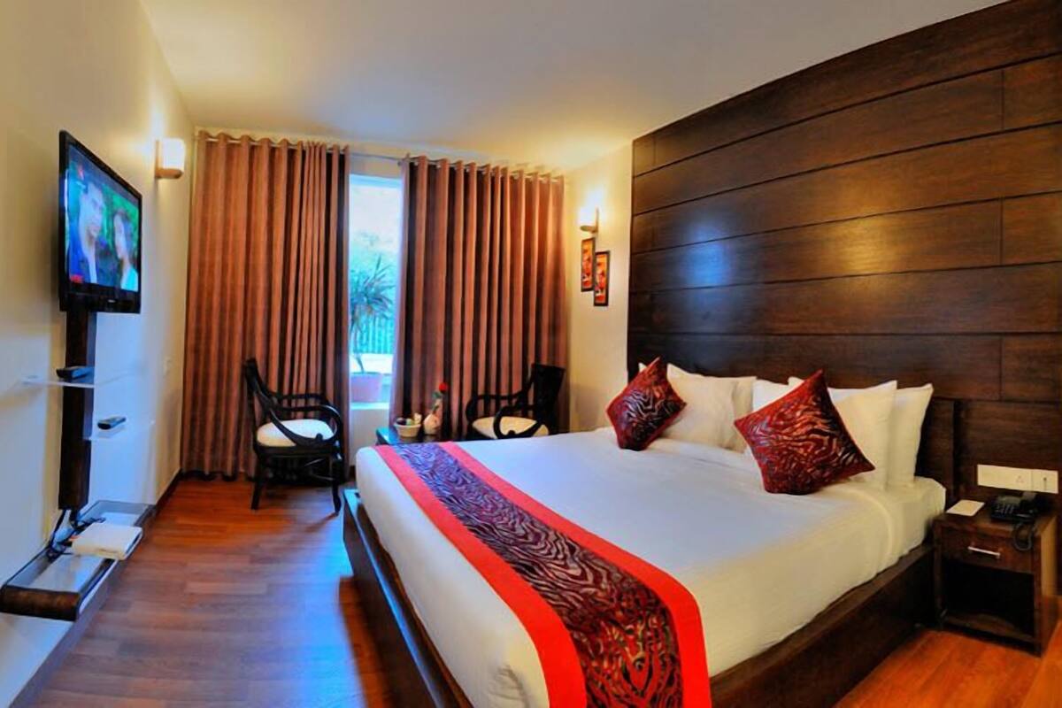 A hotel room with a large bed, wooden headboard, a TV on the wall, and a desk with a chair.