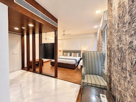 A modern hotel room with a bed, a TV, a sofa, and a glass coffee table.