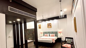 A hotel room with a bed, a desk, and a chair. There is a TV on the wall and a ceiling fan. - Hotel Atulyaa Taj (Agra)