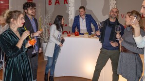 Een groep mensen tijdens een wijnproeverij, met een witte tafel waarop verschillende wijnflessen en glazen staan.