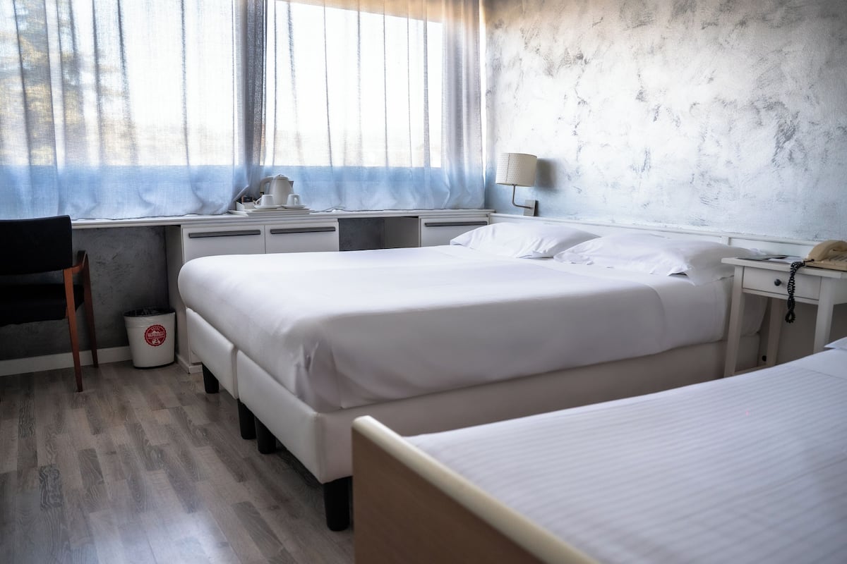 Une chambre d’hôtel avec deux lits, un bureau avec une chaise, une lampe et une poubelle.