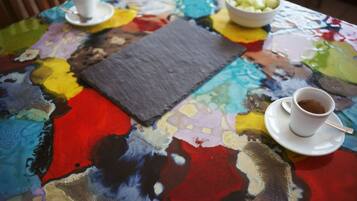 A table with a colorful abstract painting, two cups of coffee, and a bowl of fruit.