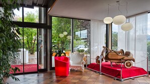 Een modern interieur met grote ramen, een rode stoel, een display van oldtimers en een rode loper.