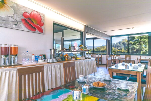 Un coin petit-déjeuner avec une grande fenêtre donnant sur le paysage, une table dressée avec des aliments pour le petit-déjeuner et un tableau accroché au mur.