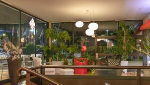 Een moderne hotellobby met een glazen gevel, kamerplanten en een zithoek met witte stoelen en een rode bank.