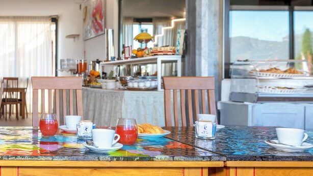 Een ontbijttafel met kopjes en een karaf, een buffet met eten, en uitzicht op de omgeving.