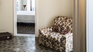A hallway with a patterned floor, a floral armchair, and a hanging light fixture. - B&B Rossocorallo (Catania)