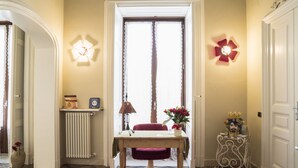 A hallway with a wooden table, a red chair, a vase with flowers, a radiator, and decorative wall lights. - B&B Rossocorallo (Catania)