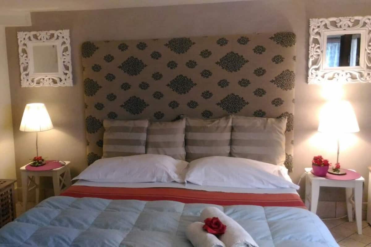 A neatly made bed with a striped bedspread, two bedside lamps, and decorative wall mirrors.