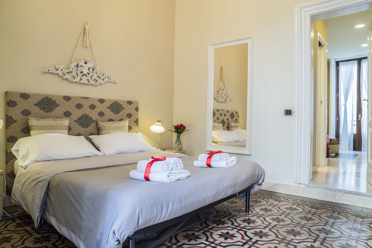 A hotel room with a bed, a nightstand, a mirror, and a patterned floor.