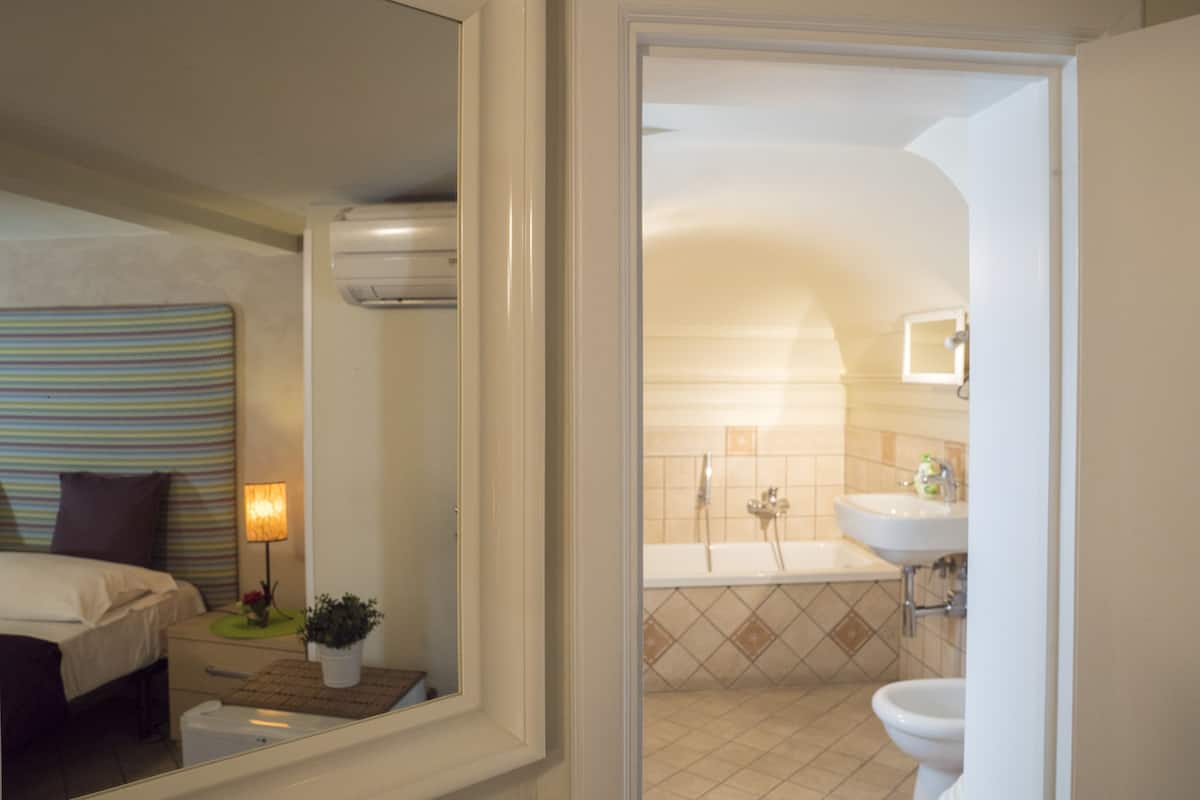 A hotel room with a bed, bedside table, lamp, and a view into the bathroom.