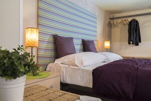 Una camera d'albergo con un letto, una lampada da comodino, una parete con un motivo a zig zag colorato e un appendiabiti con grucce.
