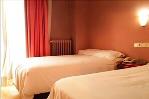 A hotel room with two beds, a red curtain, a radiator, a wall-mounted light, and a telephone on a nightstand. - Hotel Madrid Rio (Madrid)