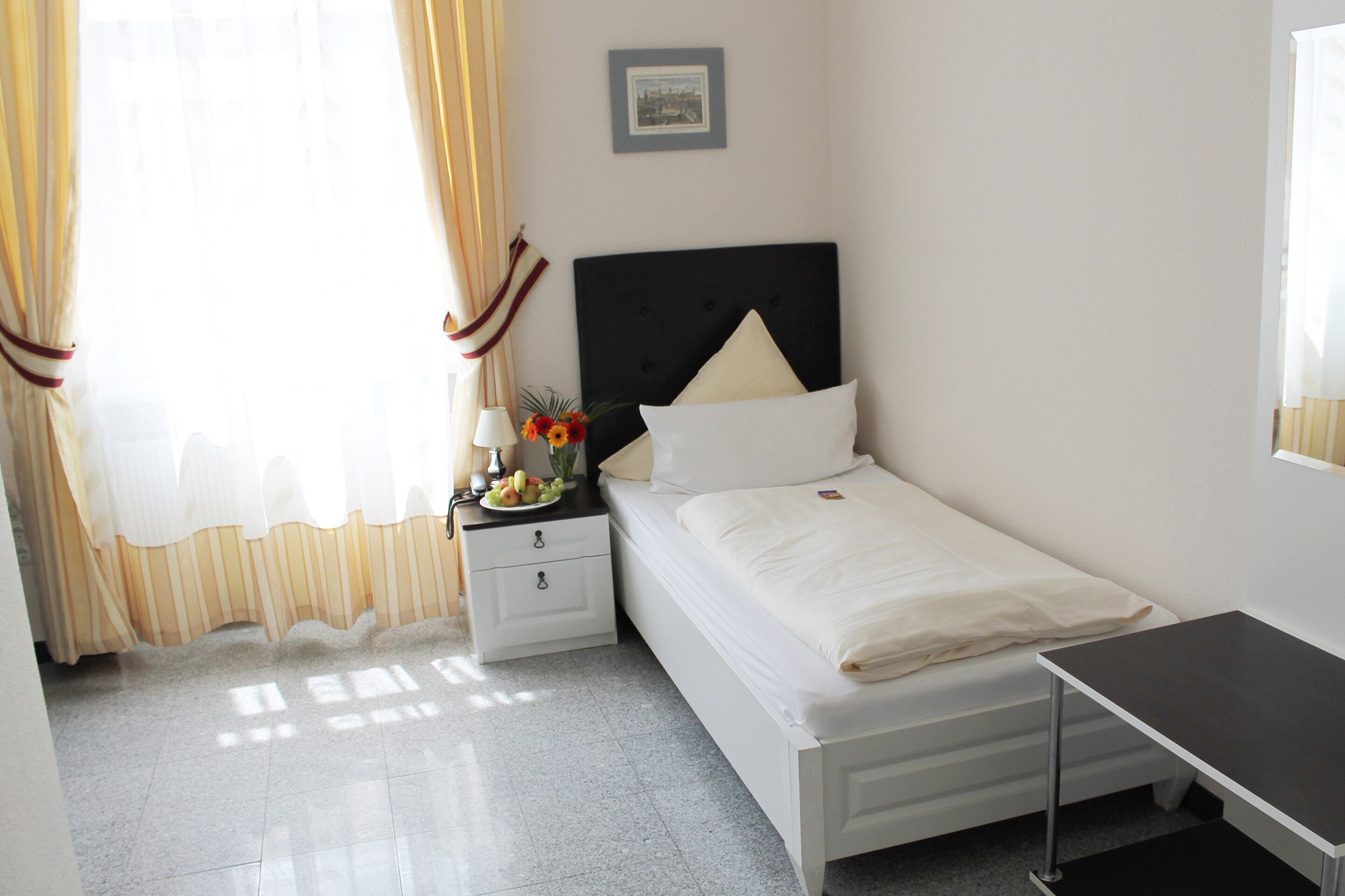 Un dormitorio ordenado con cama, mesita de noche, lámpara y una pequeña mesa.