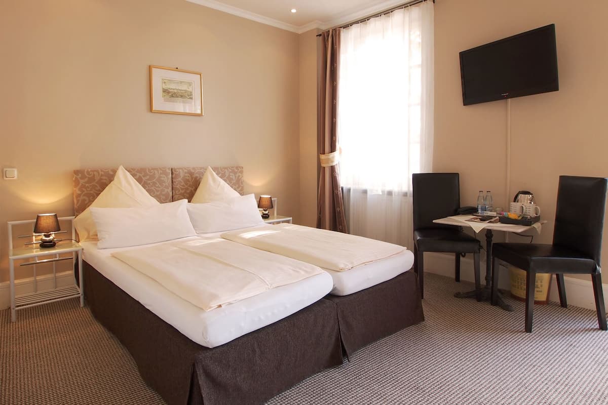 A hotel room with a bed, a desk, a chair, a TV, and a picture on the wall.