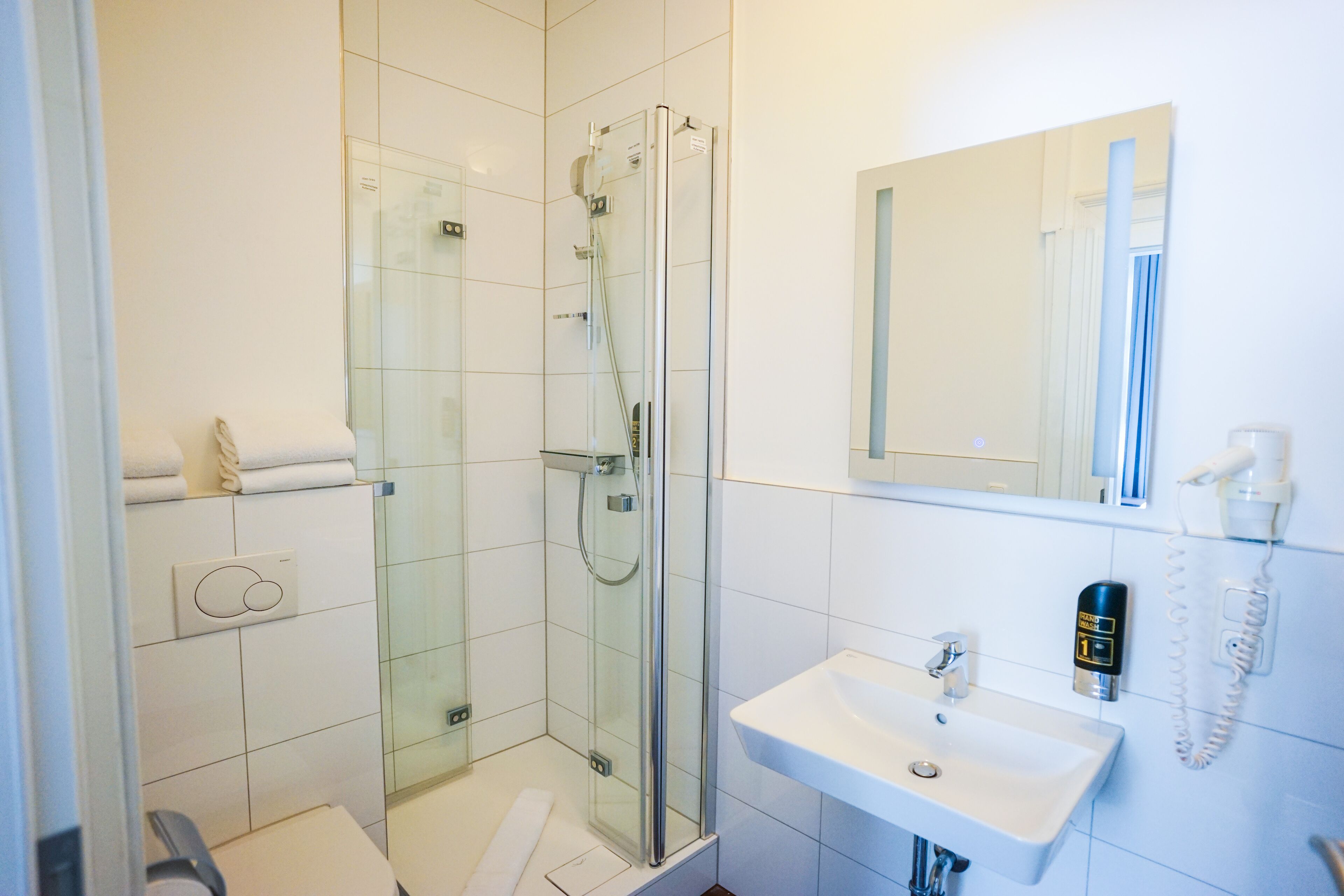 Ein modernes Badezimmer mit einer gläsernen Duschkabine, einem weißen Waschbecken und einem Spiegel darüber.