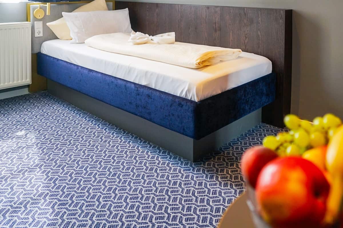 A hotel room with a bed, a blue patterned carpet, and a bowl of fruit on a table.