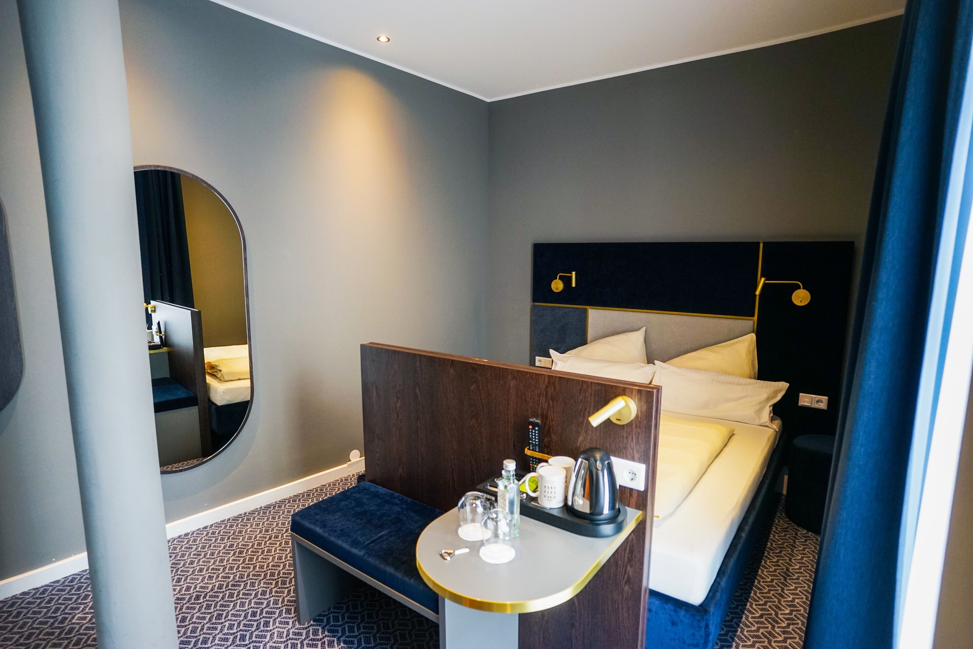 A hotel room with a bed, bedside table, mirror, and a small seating area.