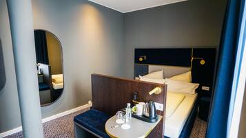 A hotel room with a bed, bedside table, mirror, and a small seating area.