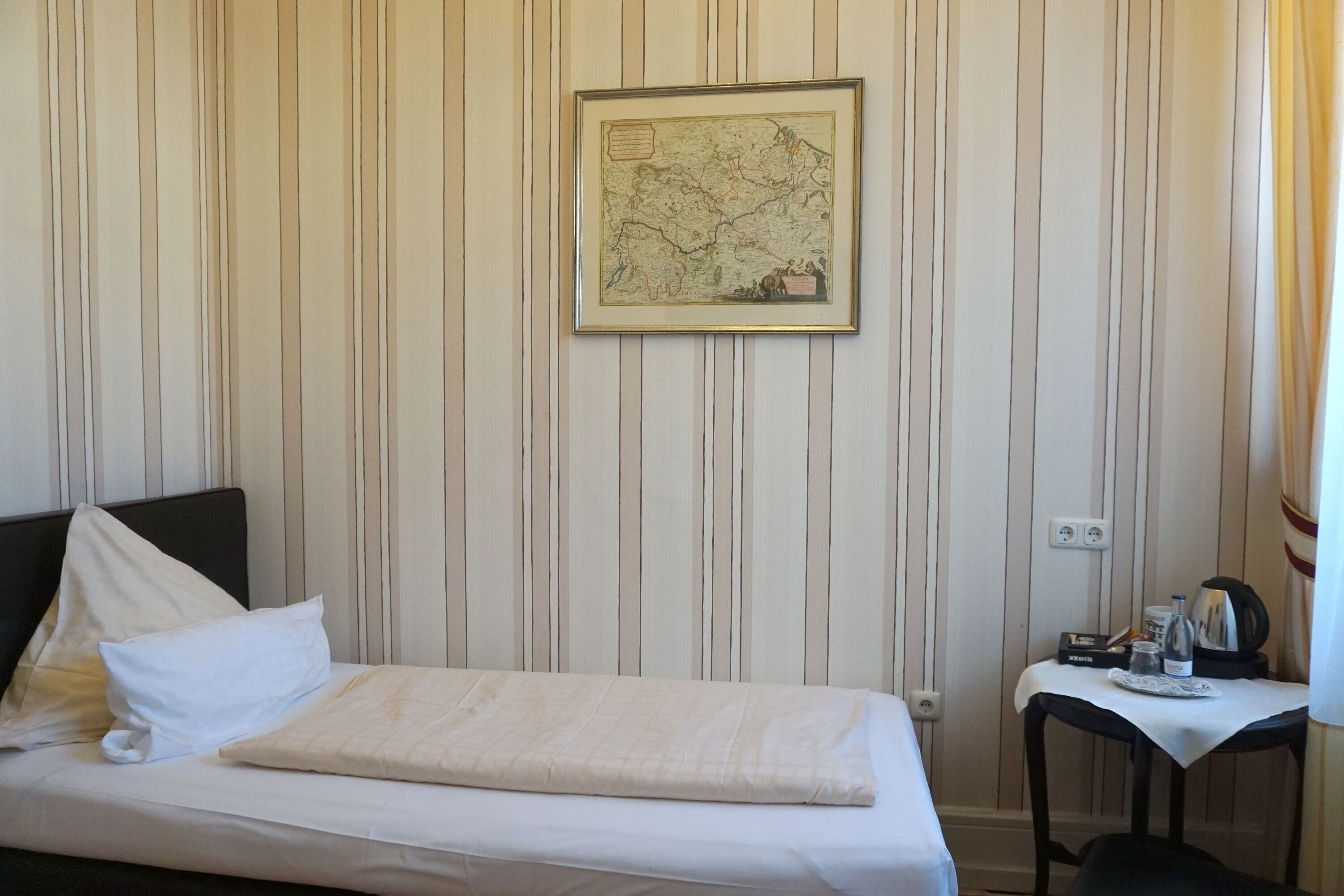 Una habitación de hotel con una cama, una mesita con una tetera y un mapa enmarcado en la pared.