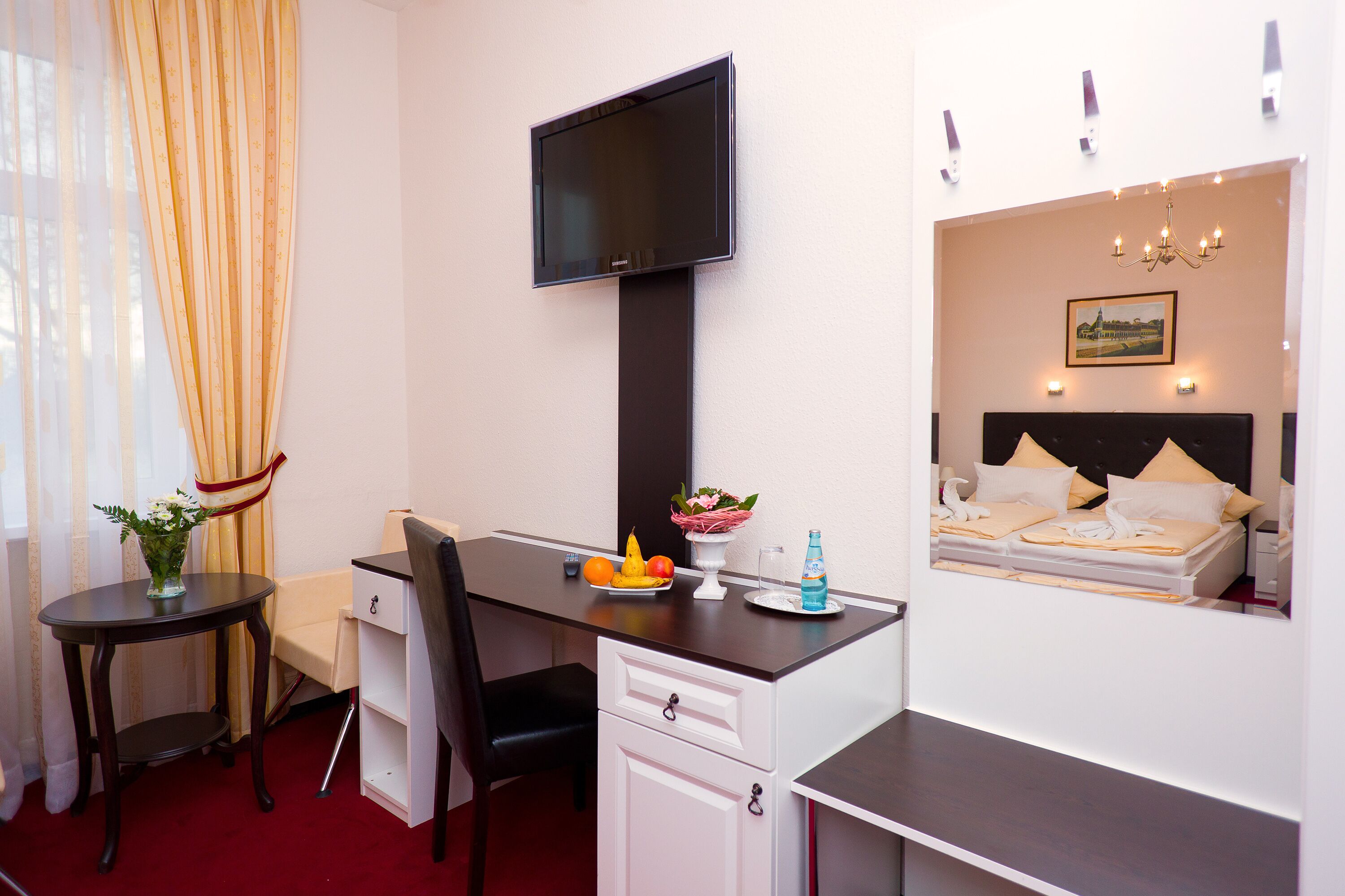 Habitación de hotel con escritorio, silla, televisión, cama y una mesita con frutas y flores.